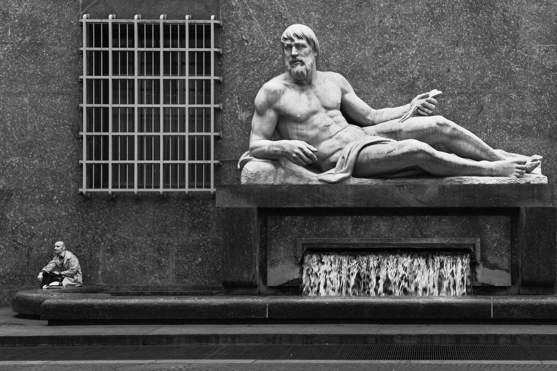 Una statua distesa e un uomo seduto ai suoi piedi, fotografia di Roberto Lugano